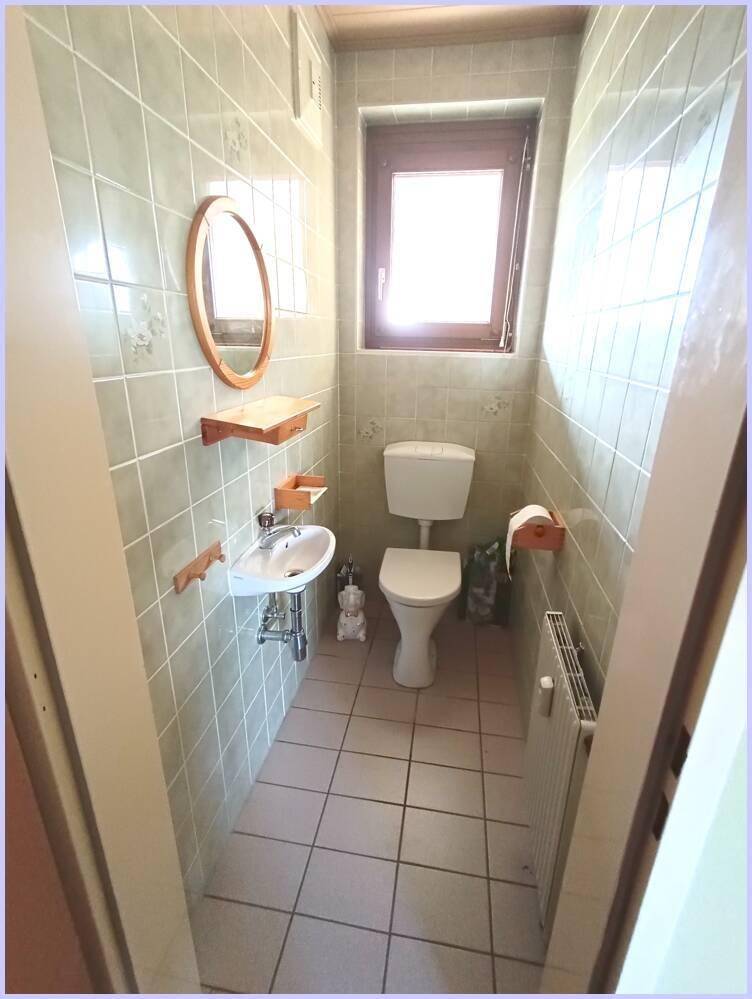 Kleines Gäste-WC mit Fenster, Toilette, Waschbecken und hellen Fliesen.