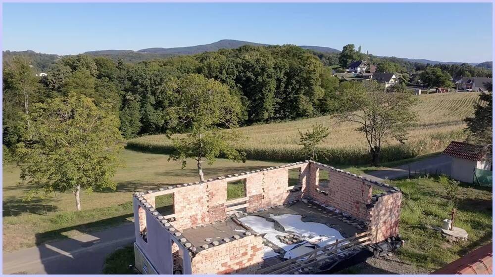Blick auf eine teilweise abgerissene Ziegelstruktur mit weitem Blick über Felder und Wälder.