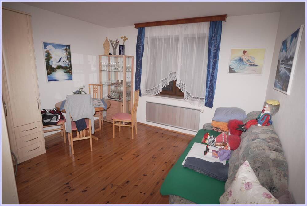 Wohn- und Essbereich mit Holzboden, Esstisch und Sofa, dekoriert mit blauen Vorhängen und Bildern.