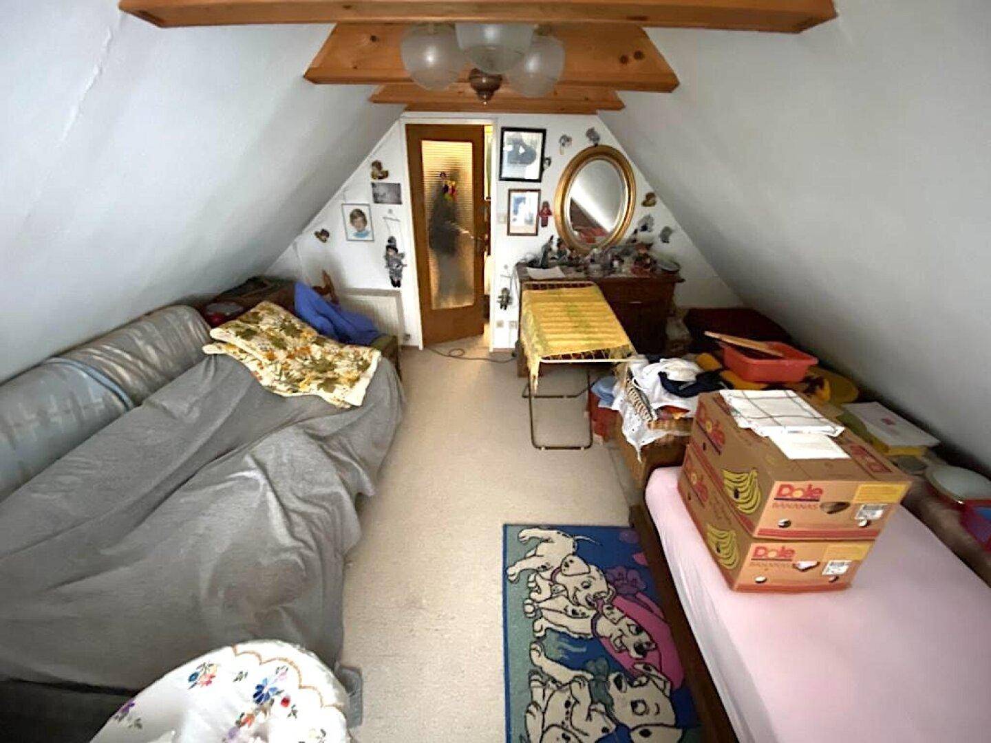 Dachzimmer mit schrägen Wänden, genutzt als Schlaf- und Abstellraum.