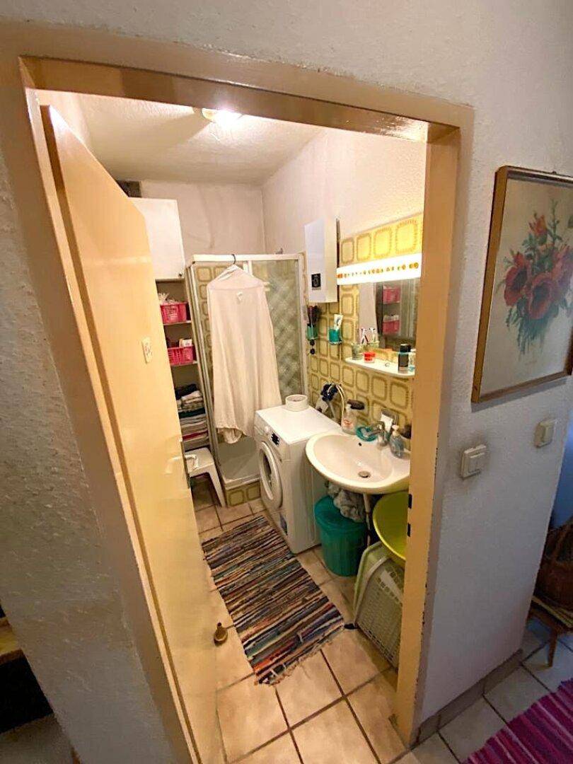 Kleines Badezimmer mit Dusche, Waschbecken, Waschmaschine und gemusterten Fliesen.