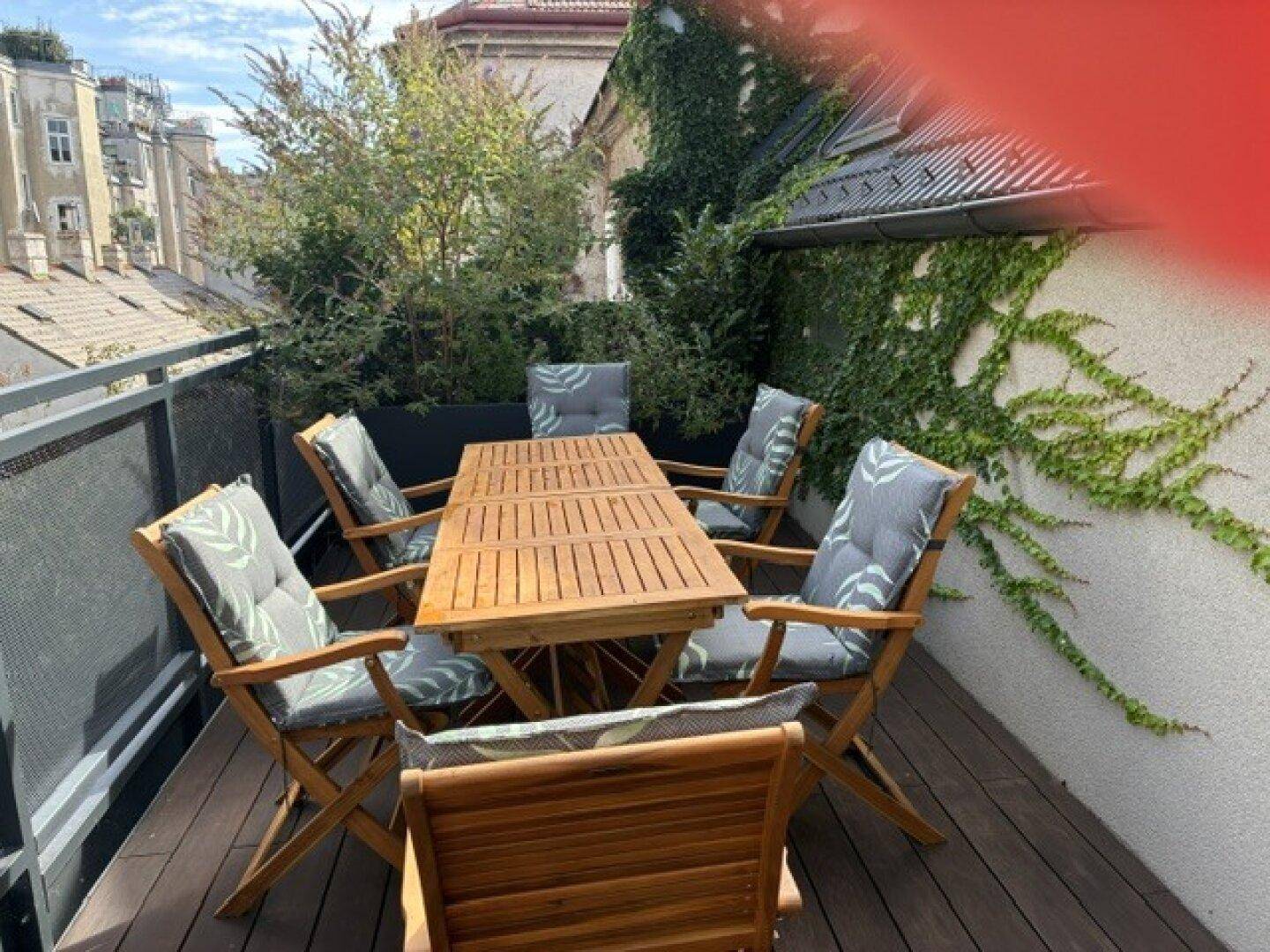 Möblierte Dachterrasse mit Holzboden, viel Grün und Blick über die umliegenden Gebäude.