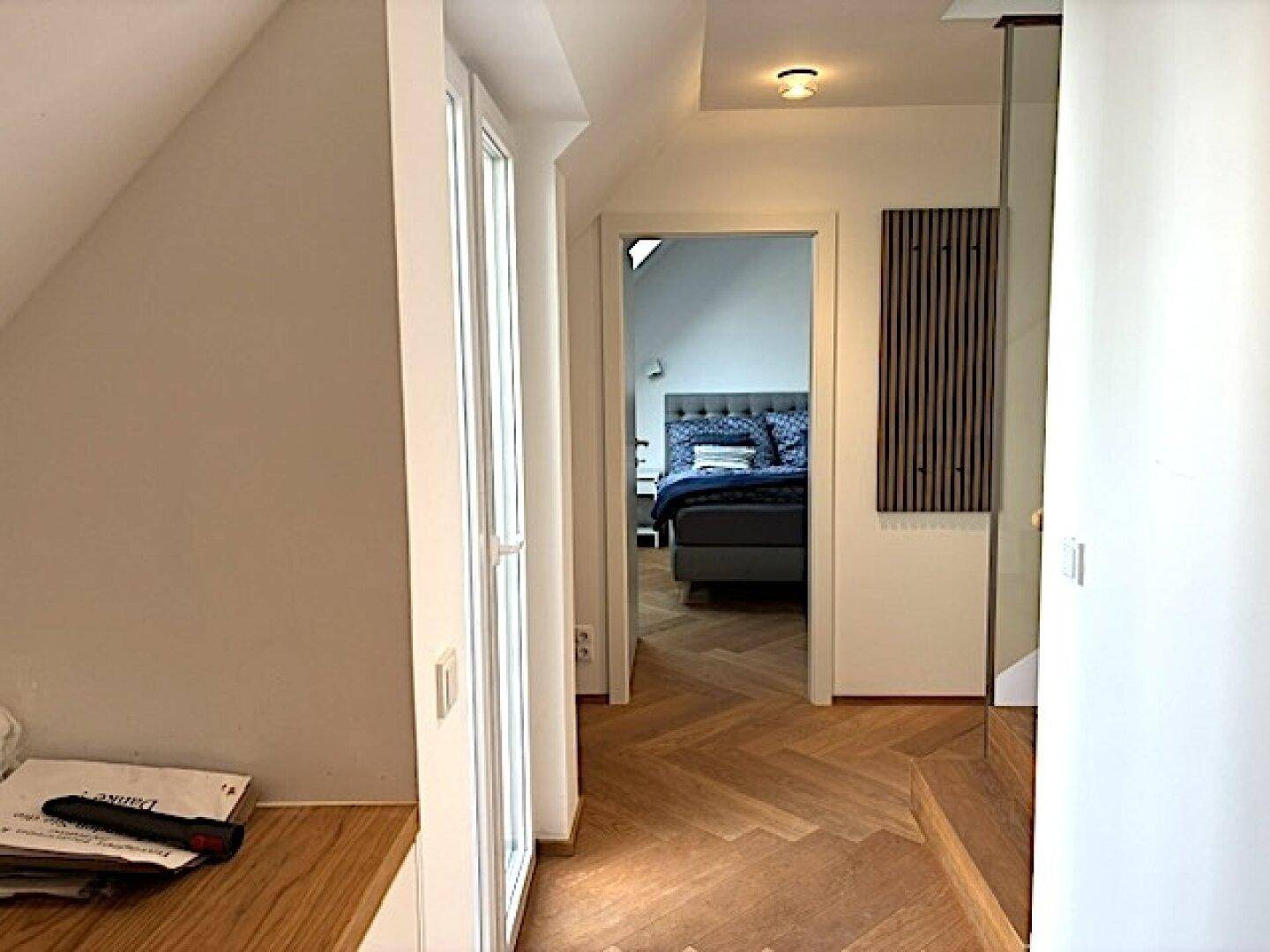 Flur mit Fischgrätparkett und Zugang zu einem Schlafzimmer im Dachgeschoss.