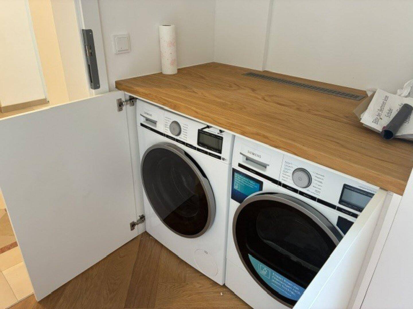 Praktischer Hauswirtschaftsraum mit integrierter Waschmaschine und Trockner unter einer Holzplatte.