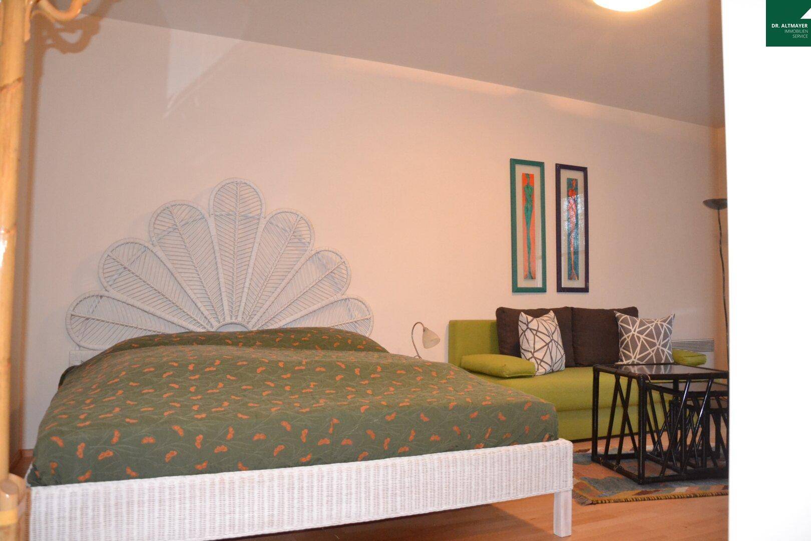 Gemütlicher Schlafbereich mit einem auffälligen weißen Rattan-Kopfteil und angrenzendem Sofa.