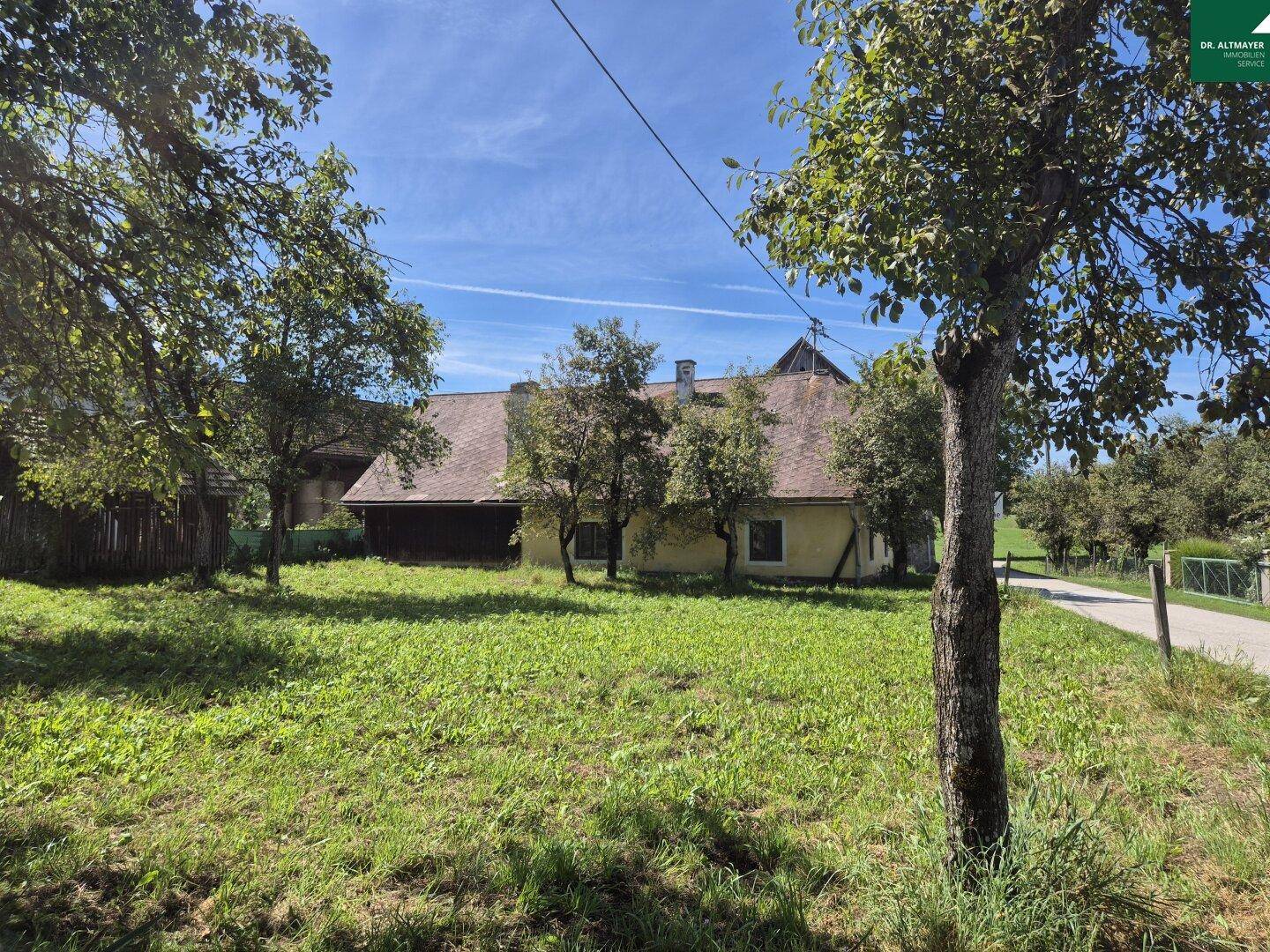 Traditionelles Haus mit braunem Dach, umgeben von einer grünen Wiese und Obstbäumen.