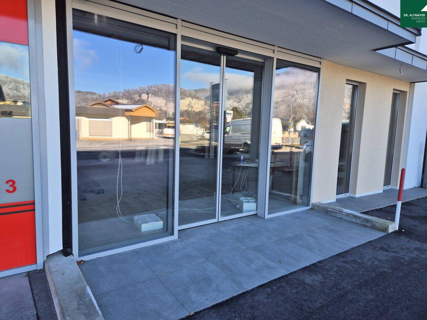 Eingangsbereich eines modernen Gebäudes mit breiter Rampe und großen Glas-Schiebetüren, die Barrierefreiheit ermöglichen.