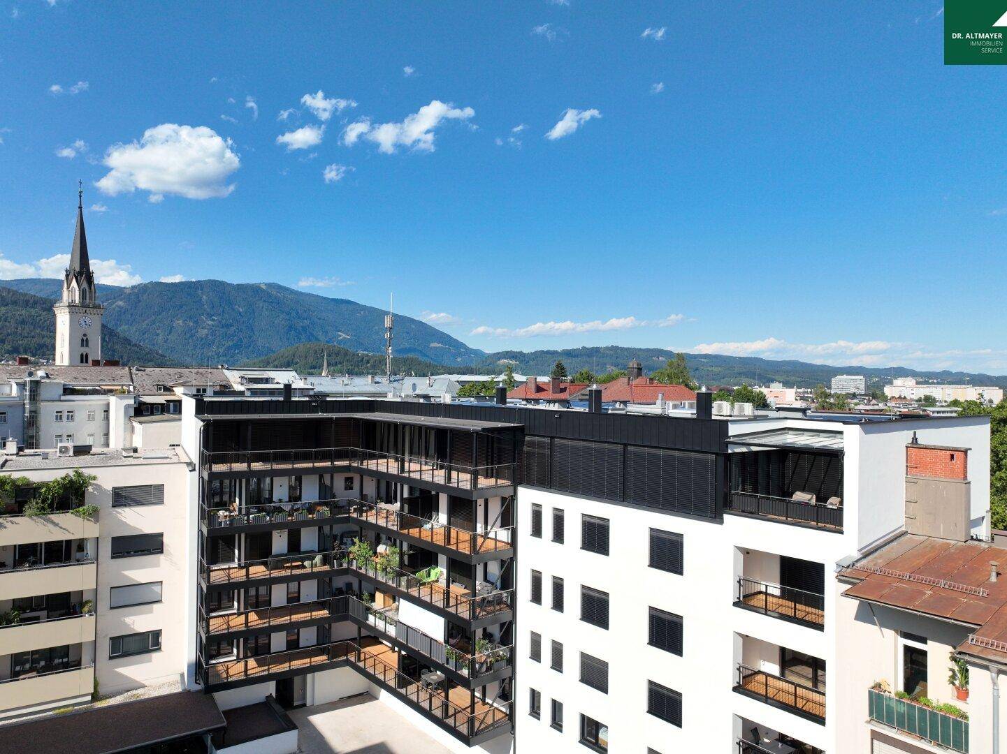 Moderne Wohngebäude mit zahlreichen Balkonen und Panoramablick auf die Stadt und die Berge.