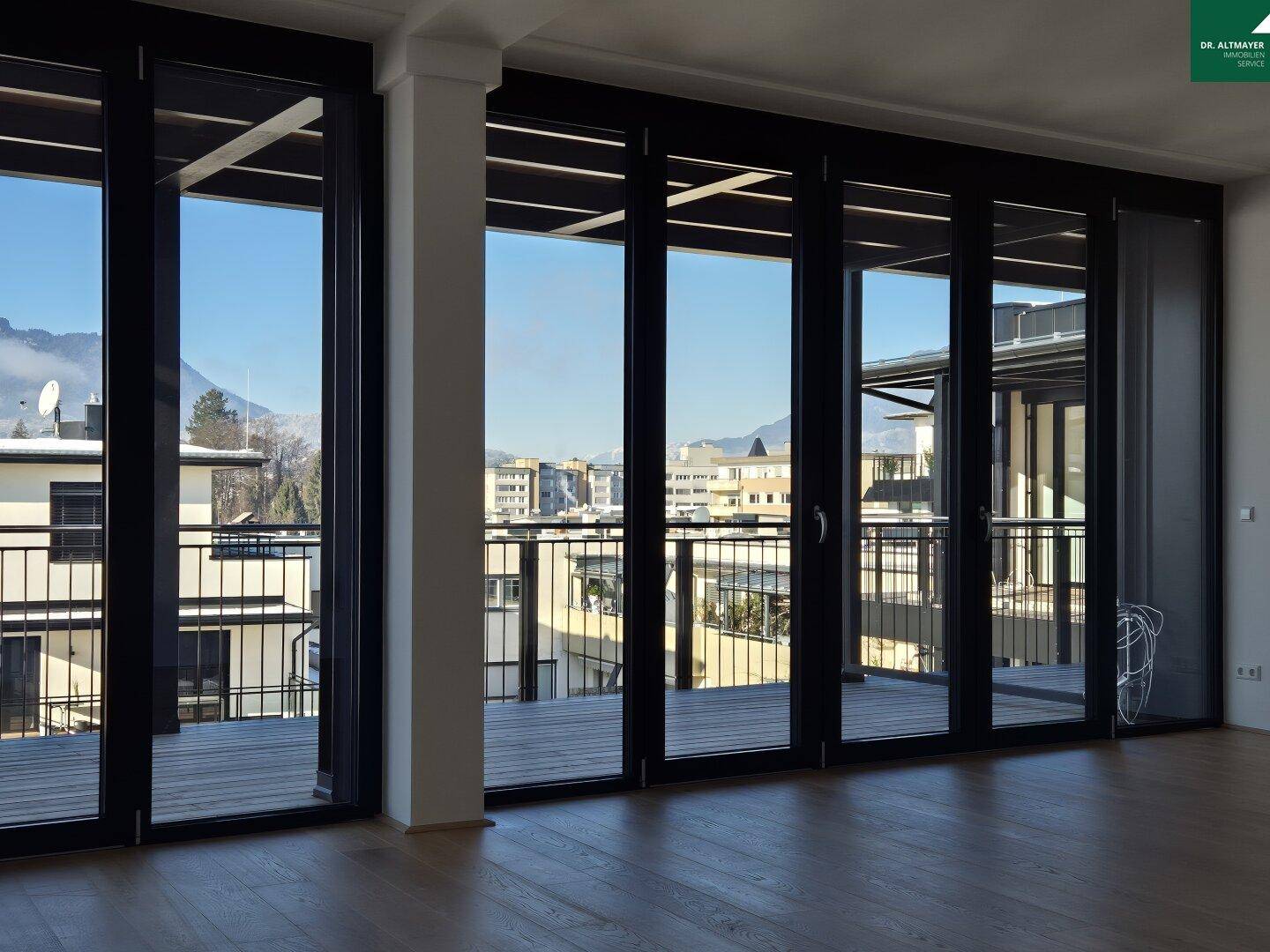 Heller Innenraum mit großen Glasfronten, Holzboden und weitem Blick auf die Stadt und Berge.