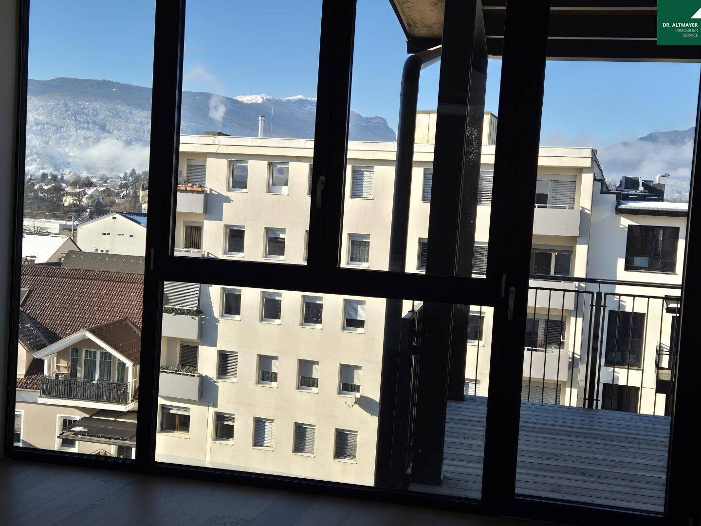 Panoramablick aus dem Fenster auf schneebedeckte Berge und umliegende Gebäude.