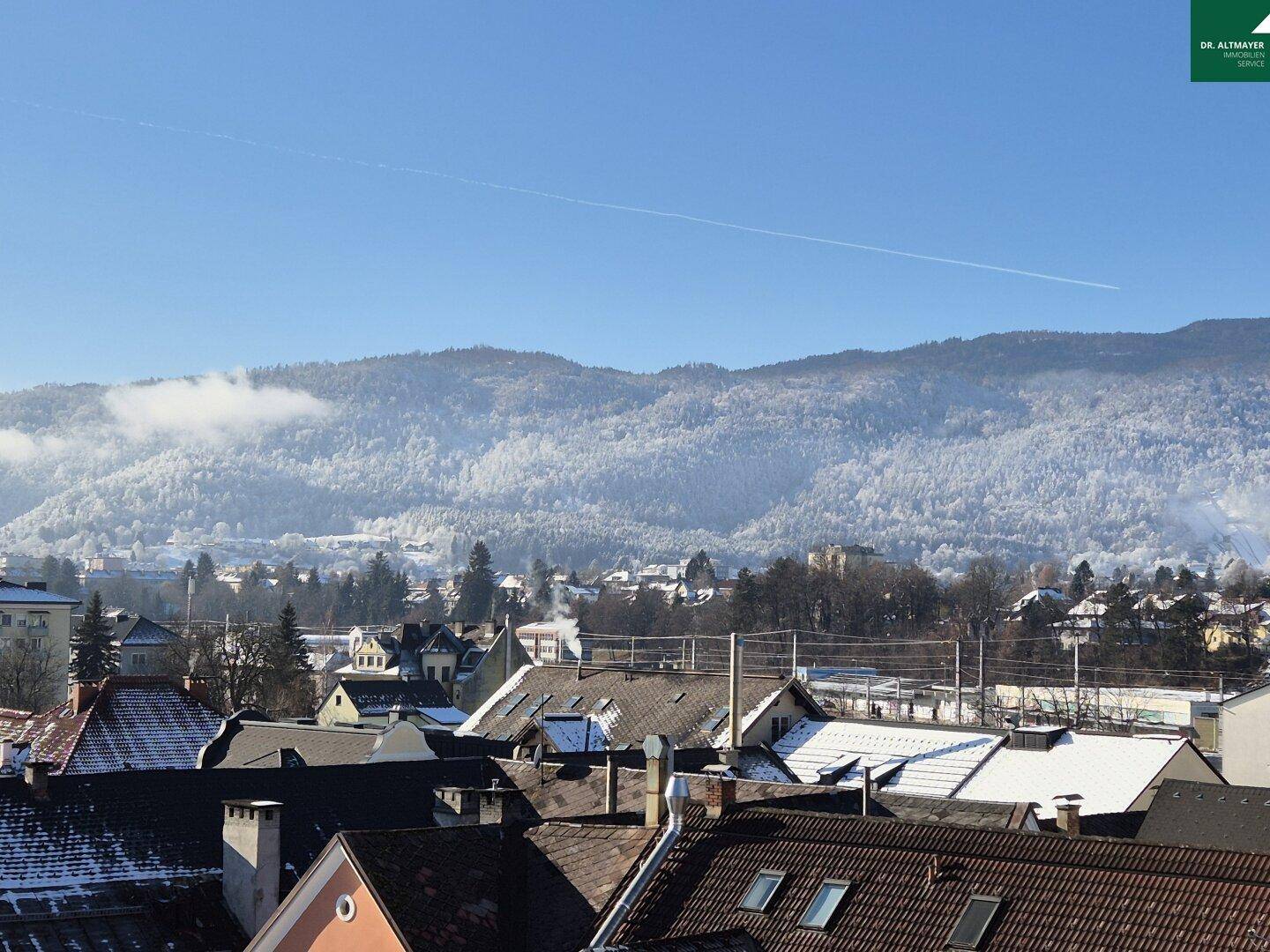 Weitläufiger Blick über verschneite Dächer und eine beeindruckende Berglandschaft.