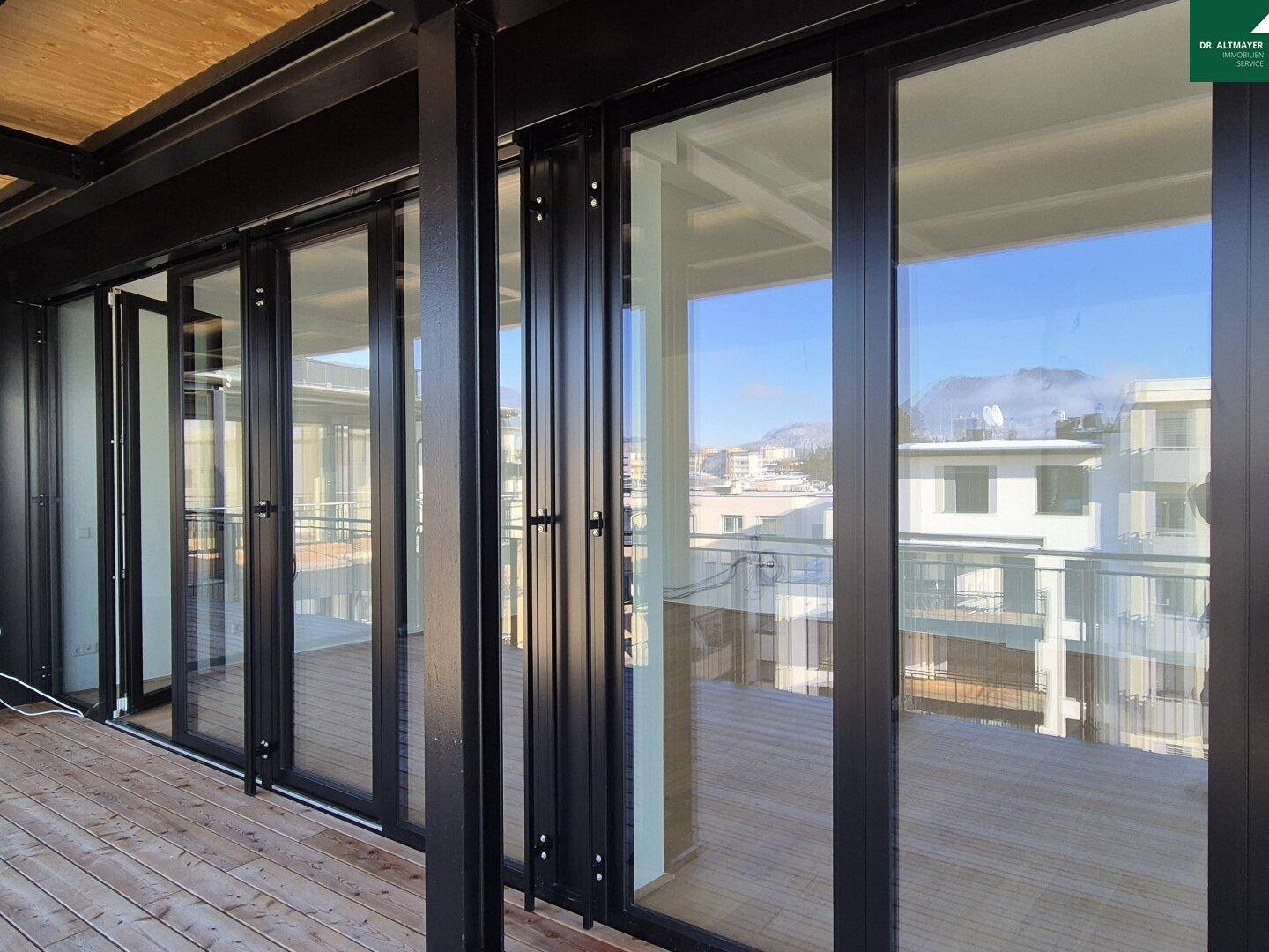 Breite Terrasse mit Glasfronten und Holzboden, die viel Licht in die Innenräume lässt.
