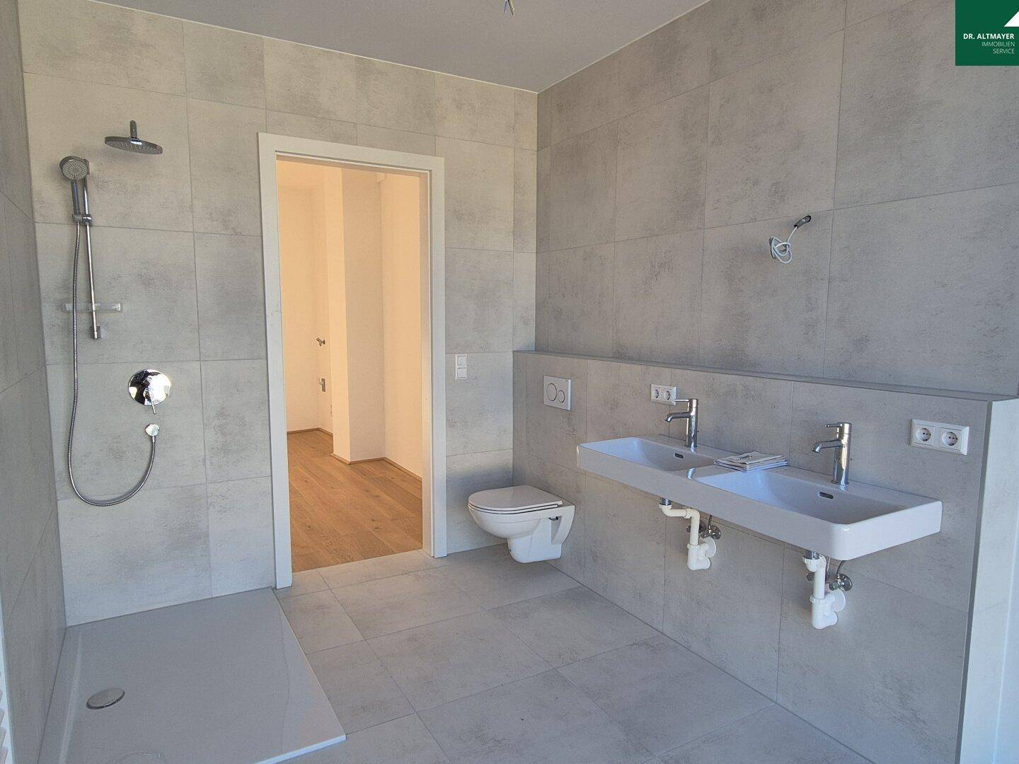 Modernes Badezimmer mit doppelten Waschbecken, ebenerdiger Dusche und hellen Fliesen.