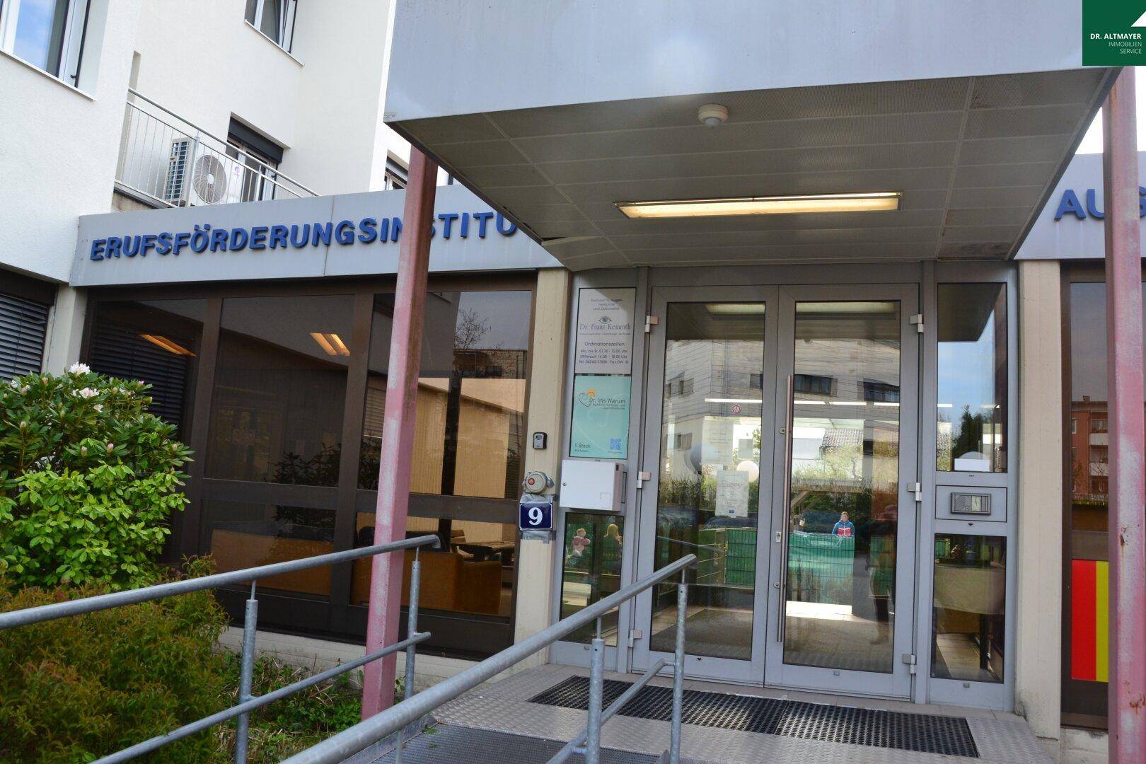 Eingangsbereich eines Gebäudes mit Glastüren und einer Rampe, gekennzeichnet als Berufsförderungsinstitut.
