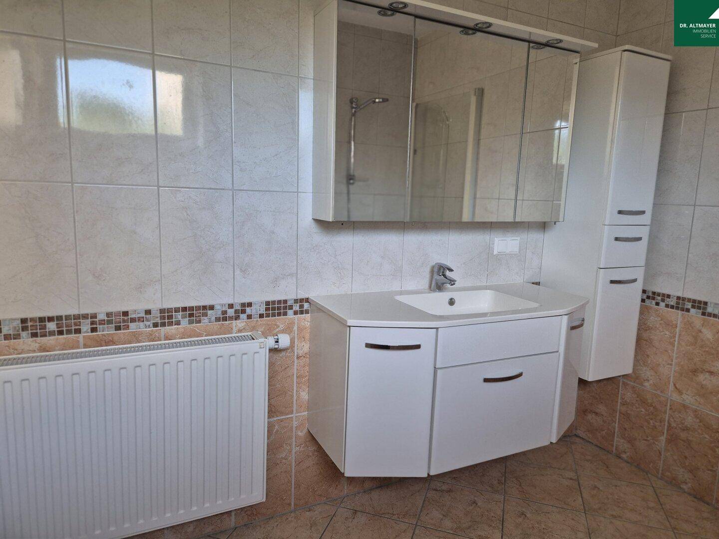 Badezimmer mit beigen Fliesen, Einzelwaschbecken, Spiegelschrank und Heizkörper.