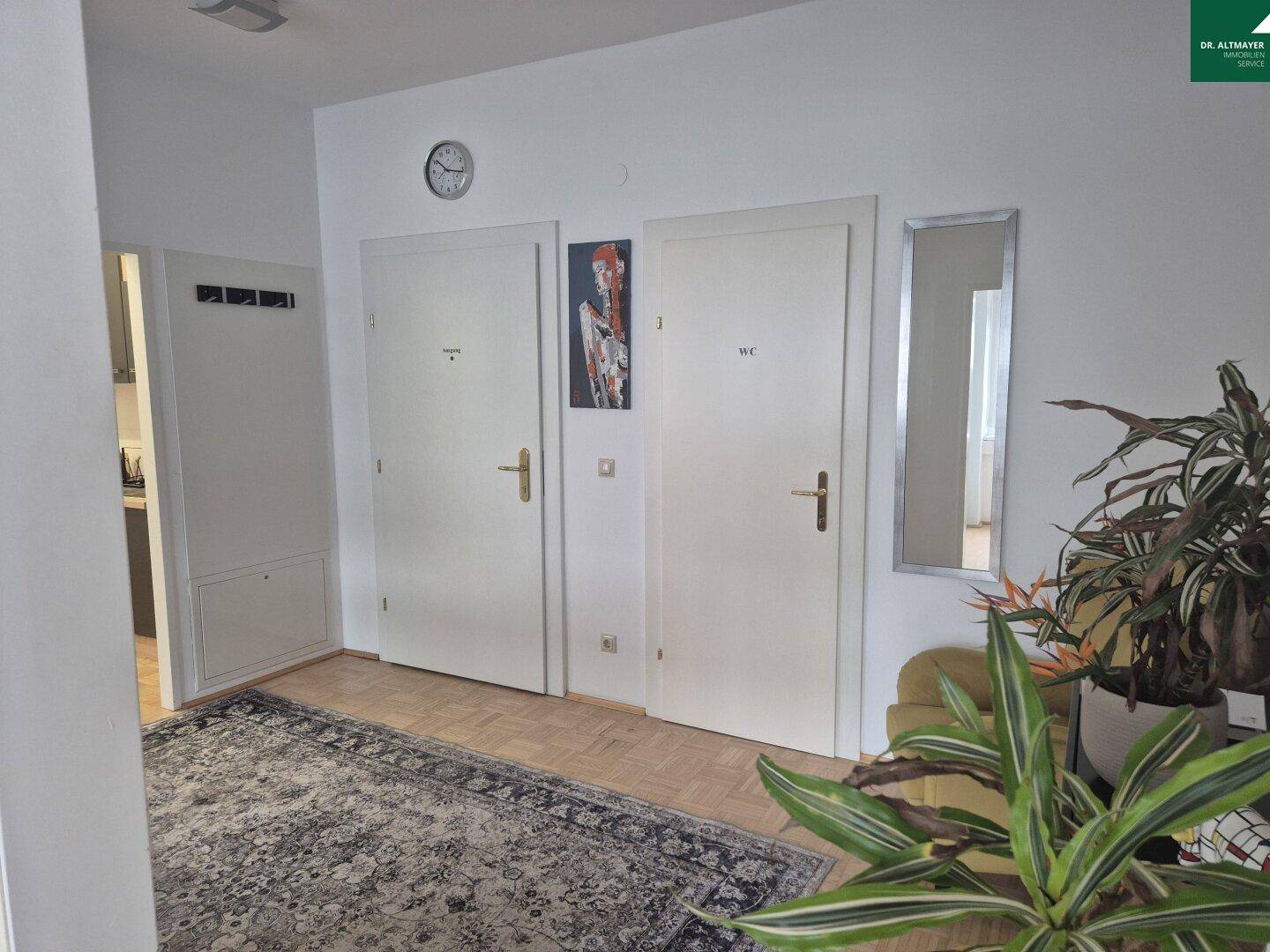 Flur mit Teppich, Pflanzen und Türen zu den Toiletten und weiteren Räumen.