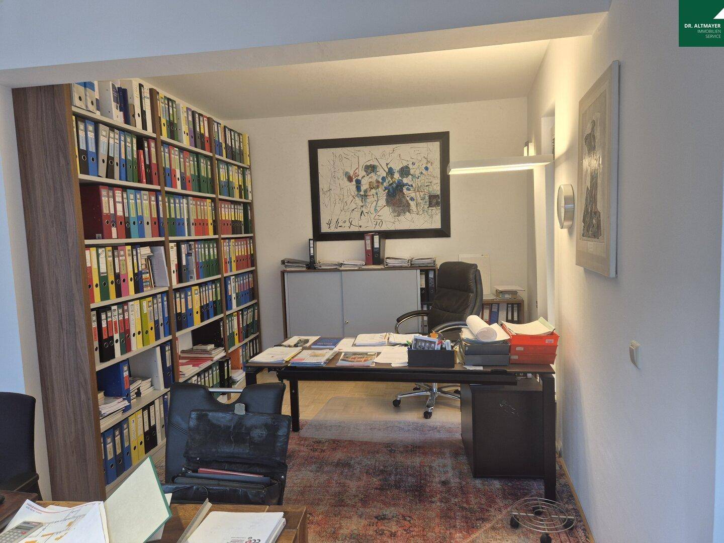 Geräumiges Büro mit großem Schreibtisch, Bürostuhl und umfangreichem Bücherregal.