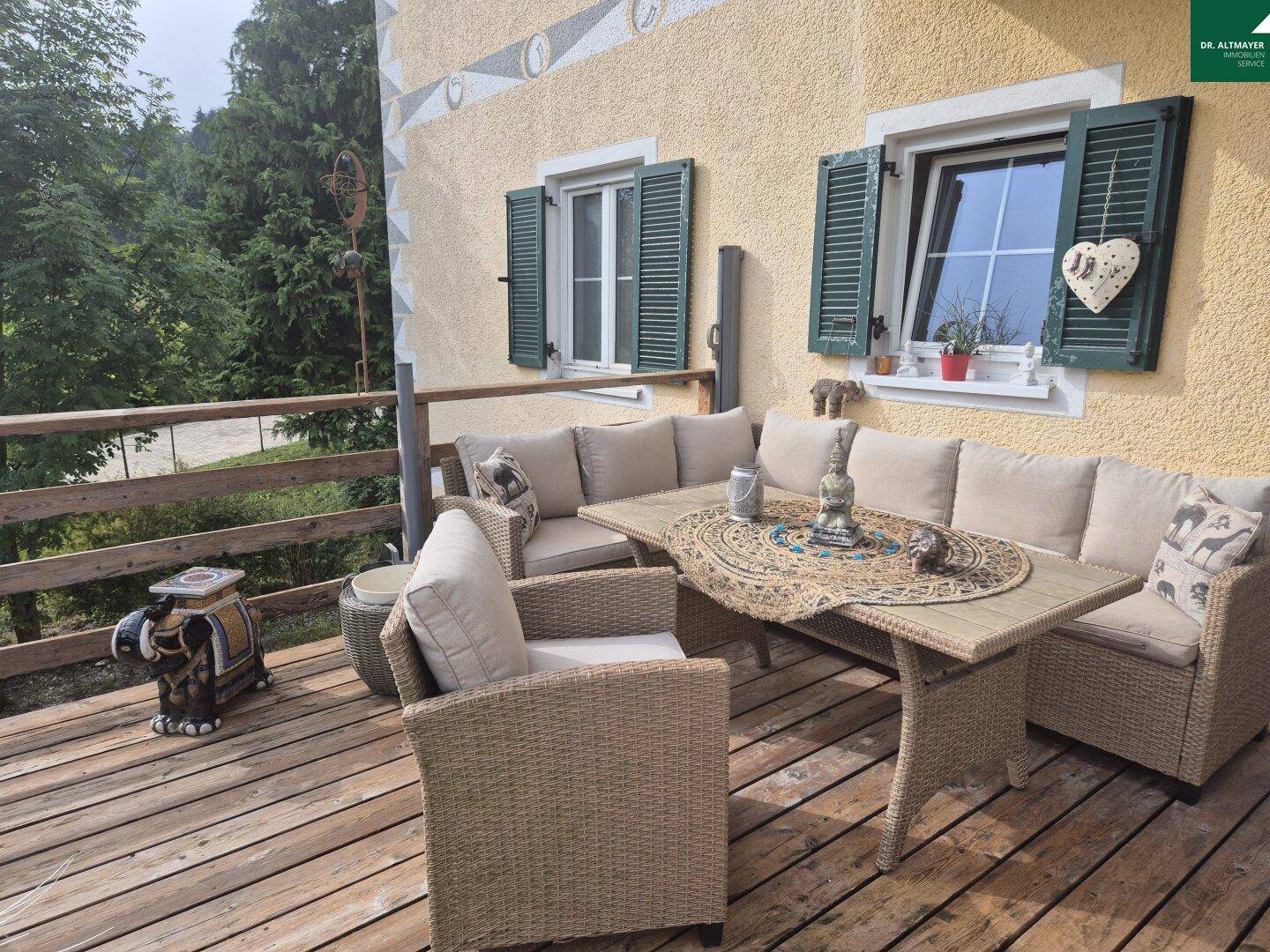 Gemütliche Holzterrasse mit Rattanmöbeln und Blick ins Grüne.