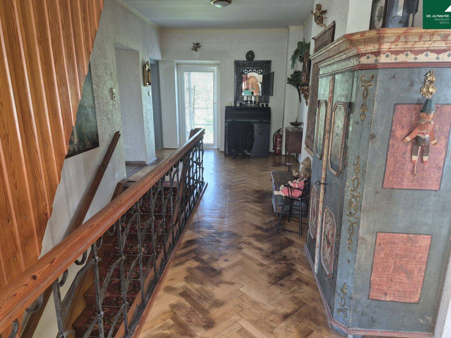 Geräumiger Flur mit Fischgrätparkett, Holztreppe und antikem Schrank.