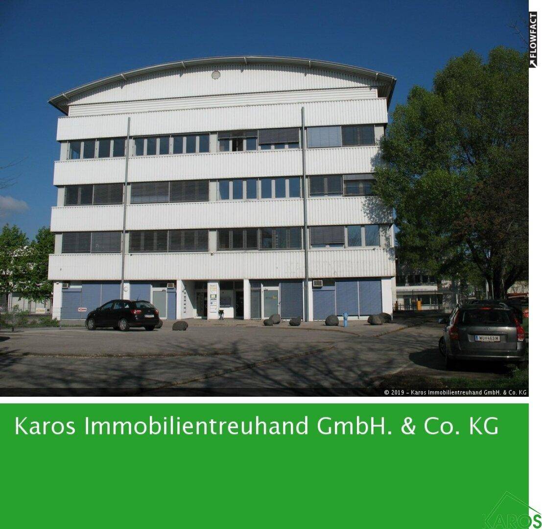 Modernes Bürogebäude mit weißer Fassade, mehreren Stockwerken und einem geschwungenen Dach, umgeben von Parkplätzen.