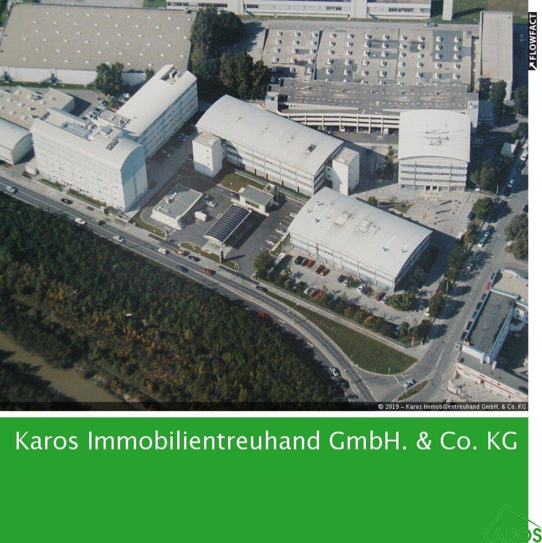 Luftaufnahme eines Gewerbegebiets mit mehreren modernen Gebäuden, Parkplätzen und umliegender Vegetation.