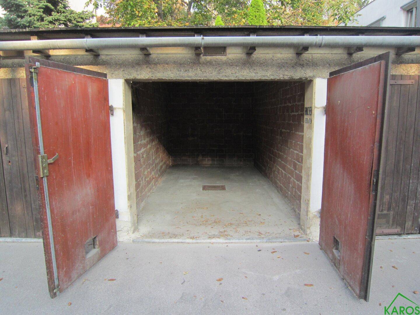 Leere Garagenbox mit geöffneten roten Toren, Ziegelwänden und einem einfachen Betonboden, bereit zur Nutzung.