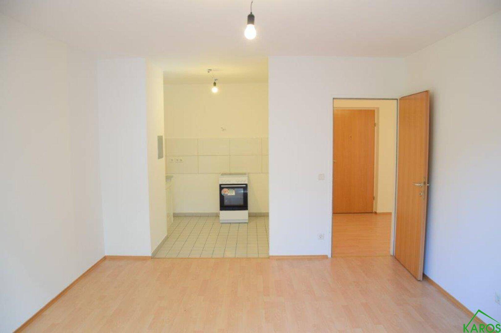 Offener Wohnbereich mit Laminatboden, der in eine geflieste Küchenzeile übergeht.