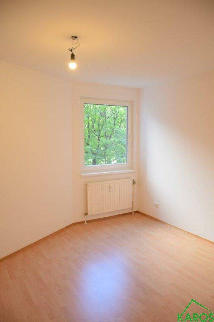 Helles Zimmer mit Laminatboden und einem Fenster, das viel Tageslicht hereinlässt.