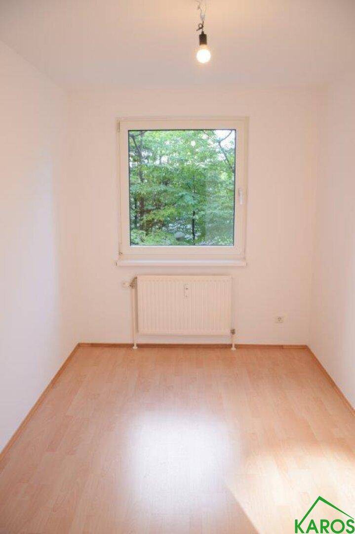 Helles Zimmer mit Laminatboden und einem großen Fenster mit Blick ins Grüne.