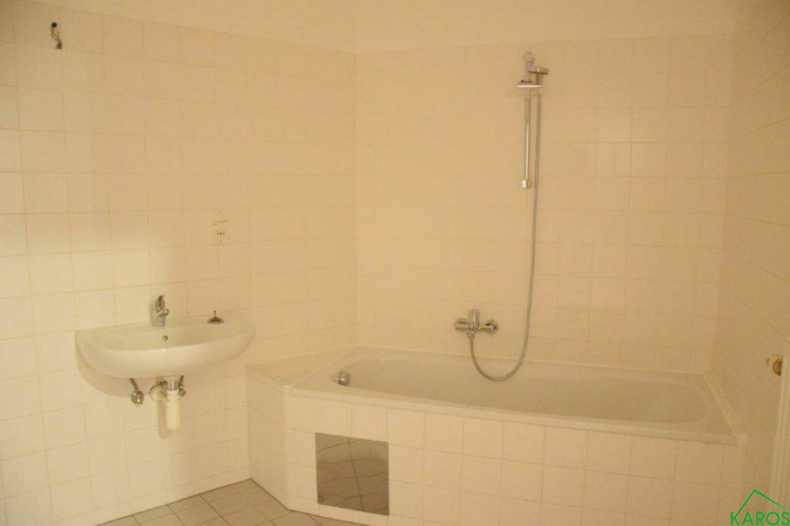 Gefliestes Badezimmer mit Badewanne, Duscharmatur und einem einzelnen Waschbecken.