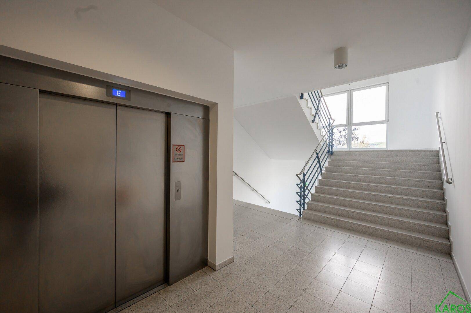Heller Treppenaufgang mit Fliesenboden und einem modernen Aufzug in einem Bürogebäude.