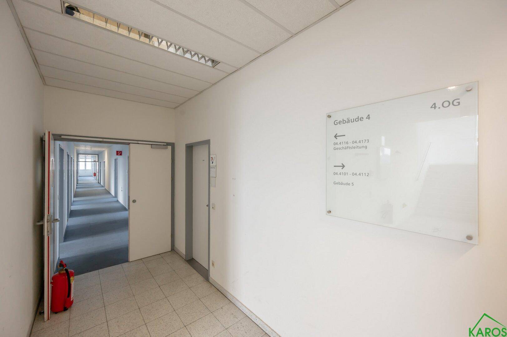 Langer Flur mit Teppichboden und Wegweiser zu den Büros im vierten Obergeschoss.
