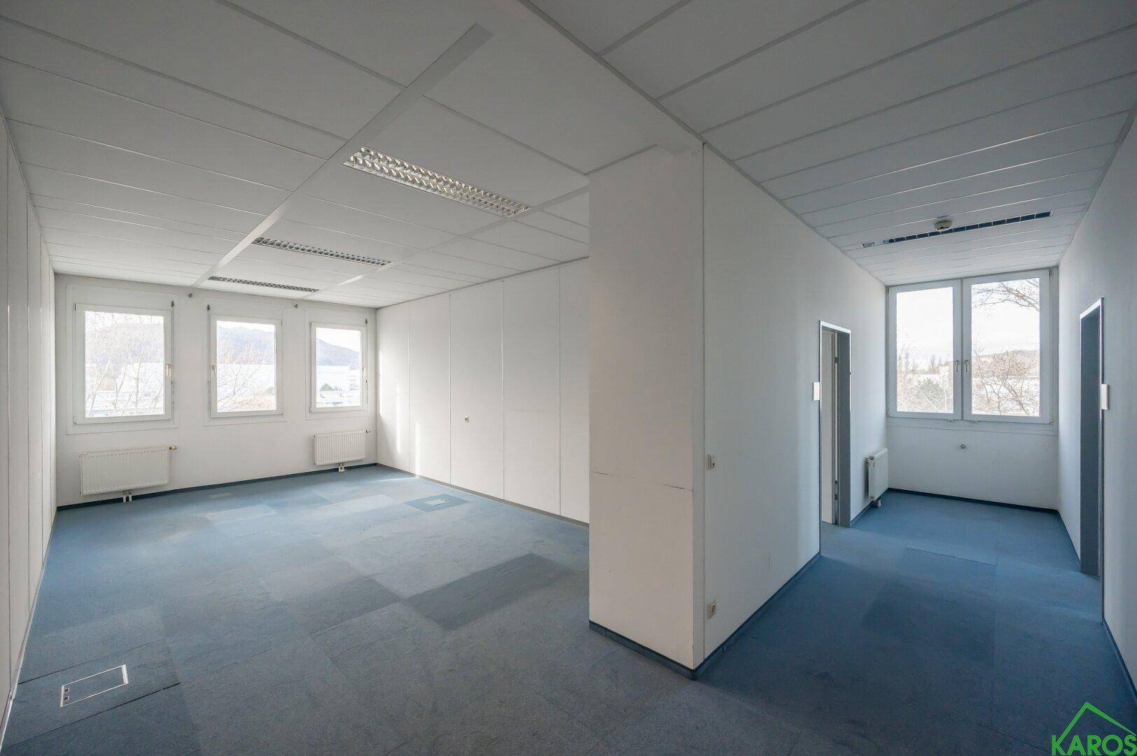 Großes Büro mit Teppichboden und Fenstern, das viel Tageslicht hereinlässt.