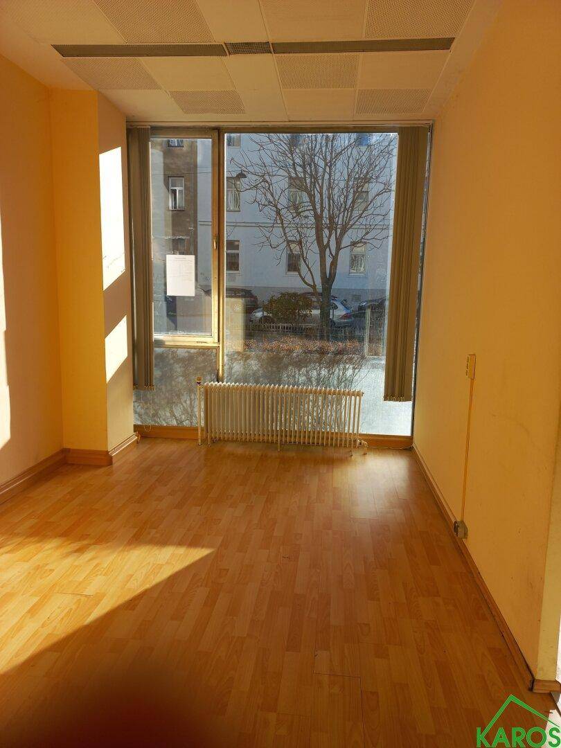 Leerer Büroraum mit großen Fenstern, Holzboden und Heizkörper, bietet viel Tageslicht.
