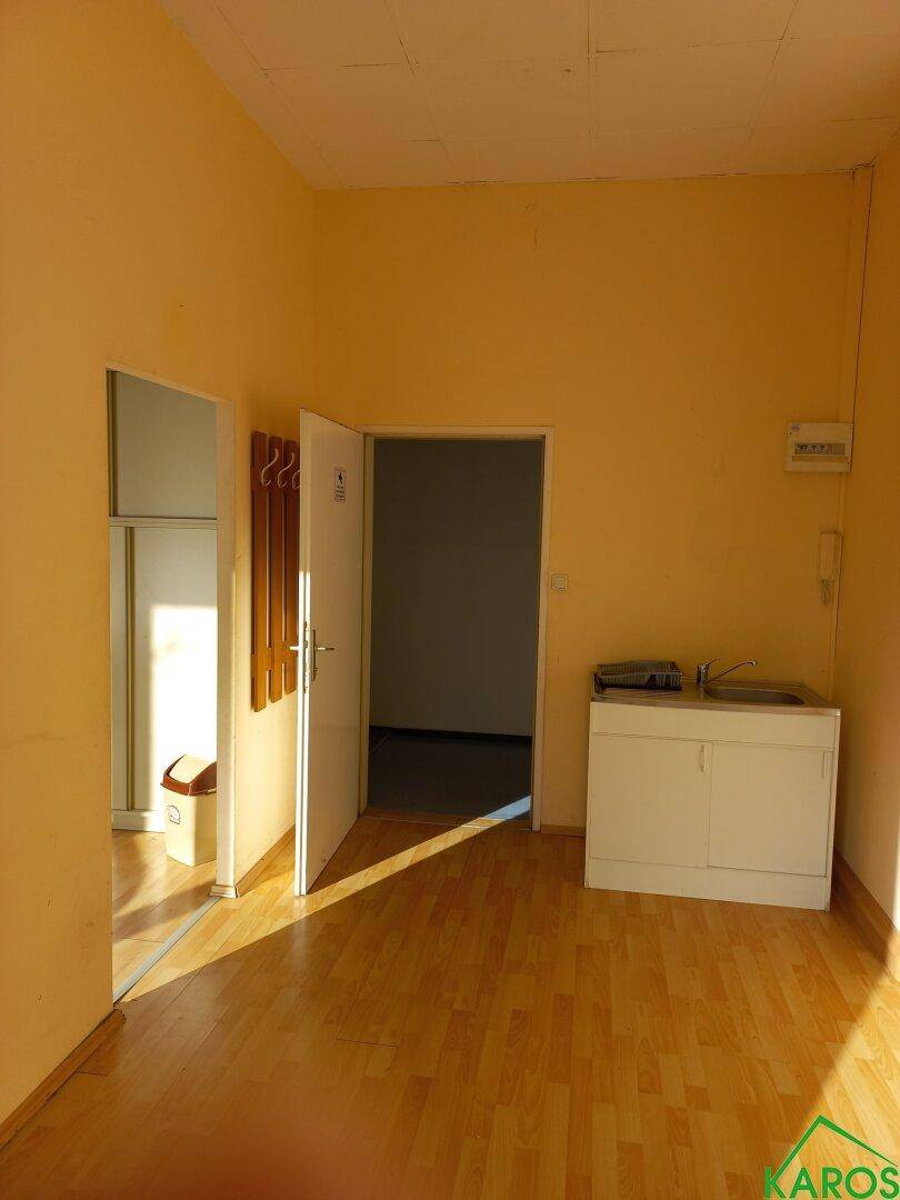 Büroraum mit kleiner Küchenzeile, Holzboden und mehreren Türen, ideal für Pausen.
