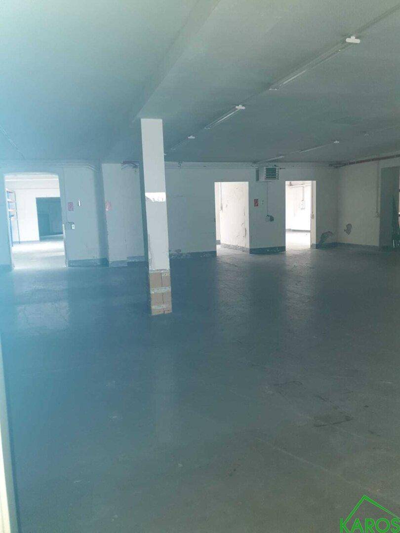 Weitläufiger, leerer Gewerberaum mit mehreren Zugängen und einer zentralen Säule.