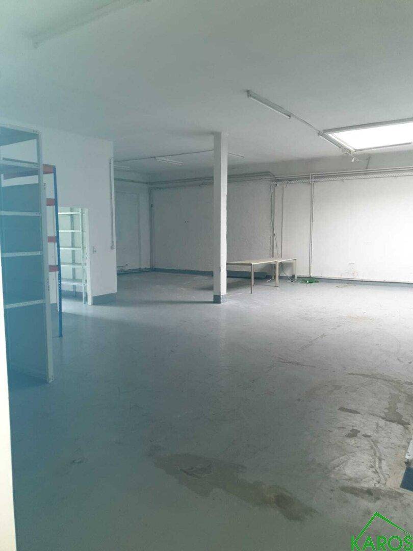 Weitläufiger, leerer Gewerberaum mit einer zentralen Säule und Deckenbeleuchtung.
