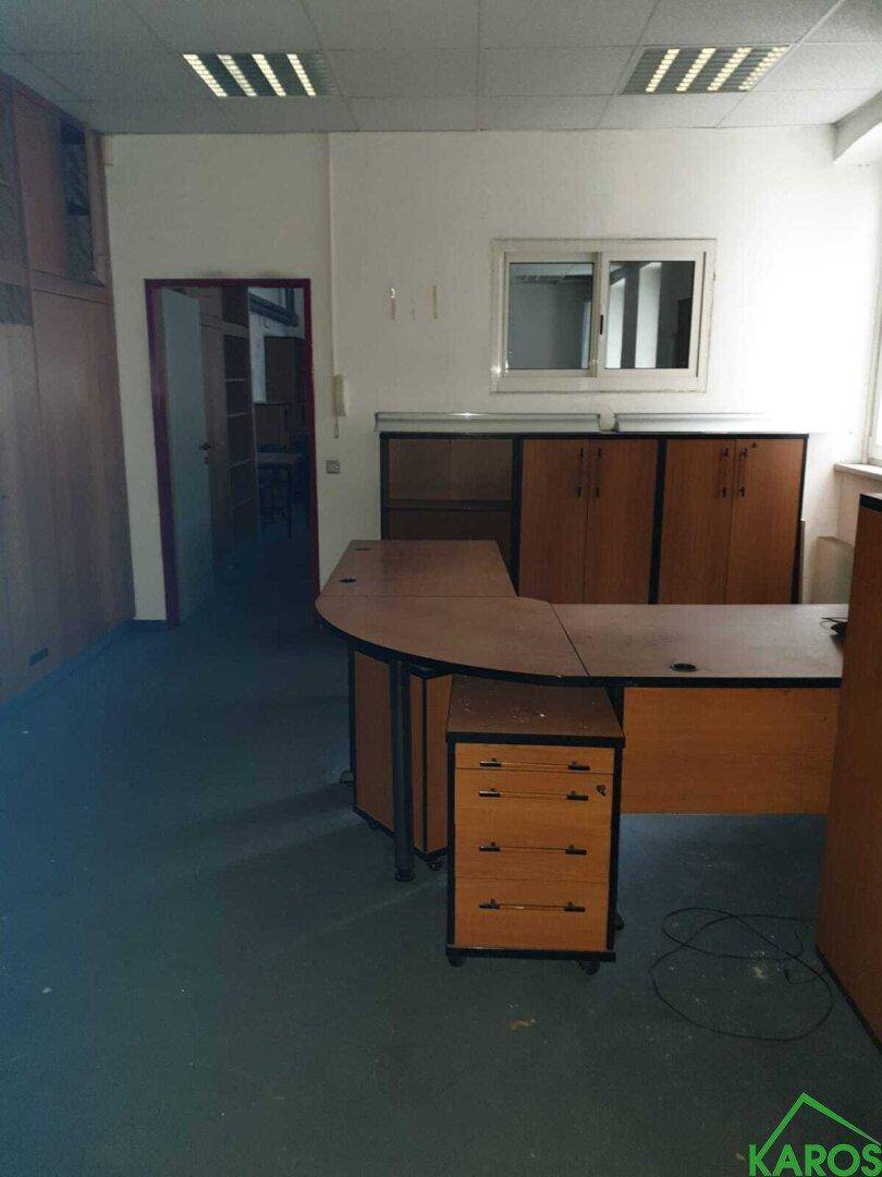 Büroraum mit Holzschreibtischen und Schränken, sowie einer abgehängten Decke.