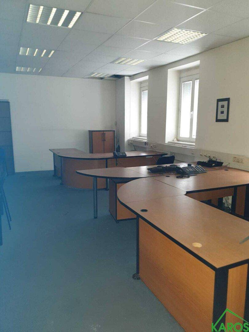Großes Büro mit mehreren Holzschreibtischen und viel Tageslicht durch die Fenster.