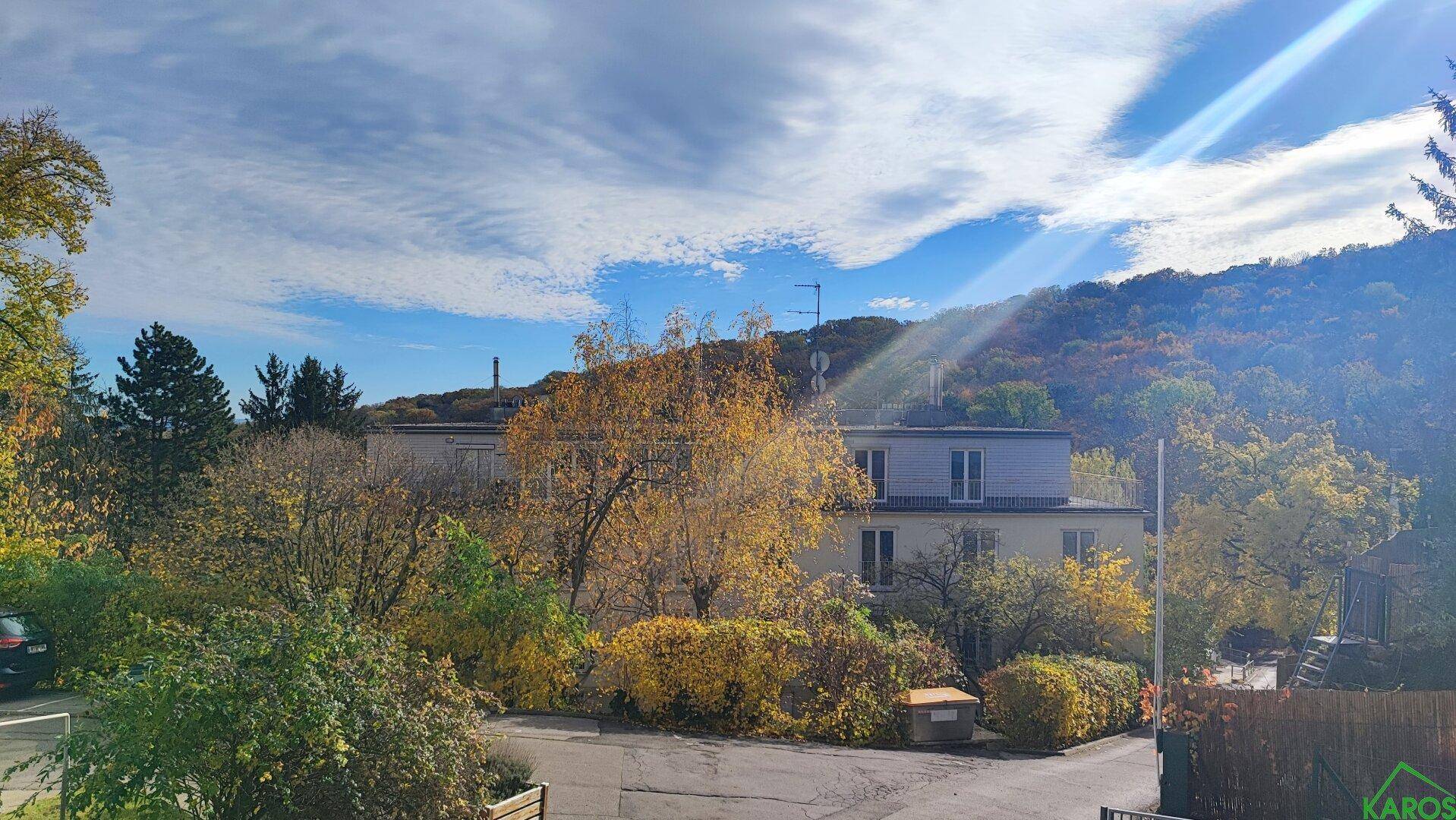 Weitläufiger Blick über die Umgebung mit einem Gebäude und bewaldeten Hügeln im Herbst.