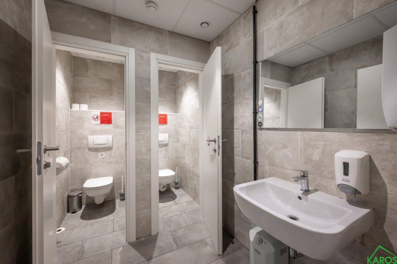 Moderner öffentlicher Waschraum mit mehreren Toilettenkabinen und einem Waschbeckenbereich.