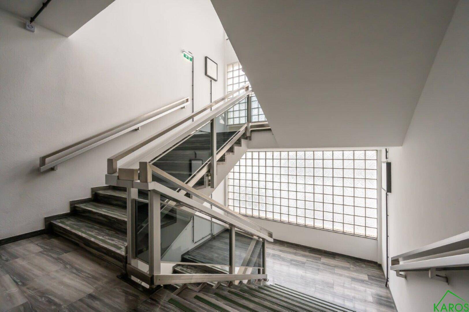 Modernes Treppenhaus mit Glasgeländer und einer Fensterwand aus Glasbausteinen.