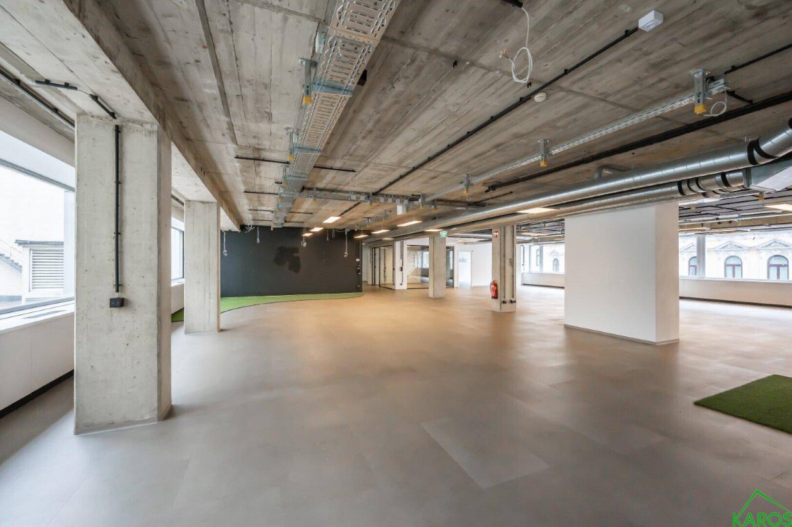 Weitläufige Bürofläche mit freiliegenden Betondecken und viel Tageslicht durch große Fenster.