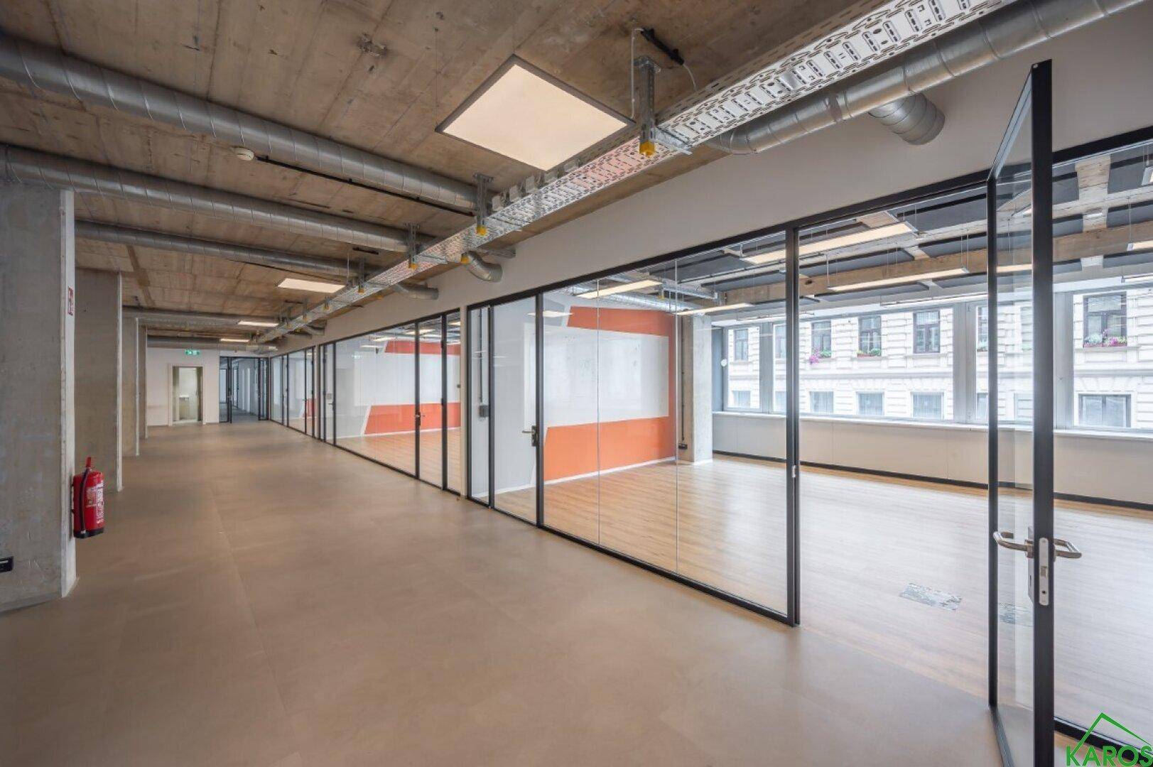Moderner Büroflur mit Glaswänden, die einzelne Büros abtrennen, und großen Fenstern.