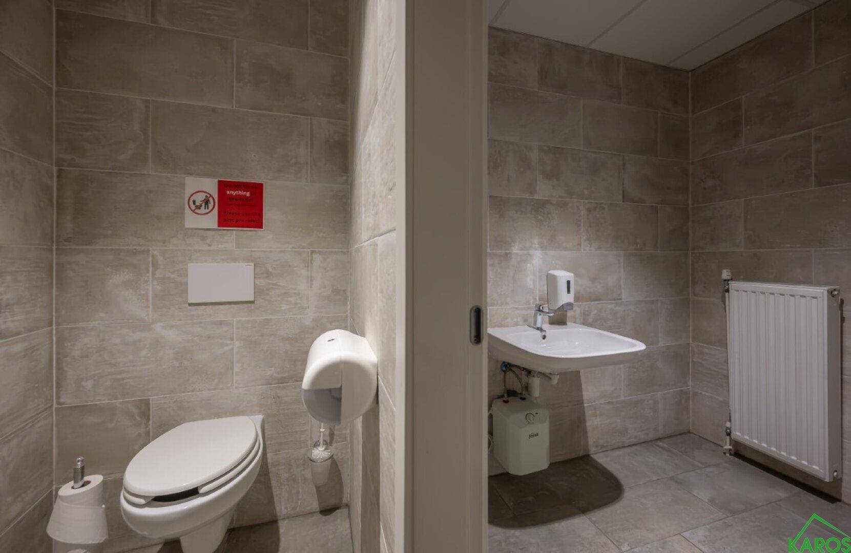 Sauberer Toilettenbereich mit Wand-WC, Waschbecken und Seifenspender in hellen Fliesen.
