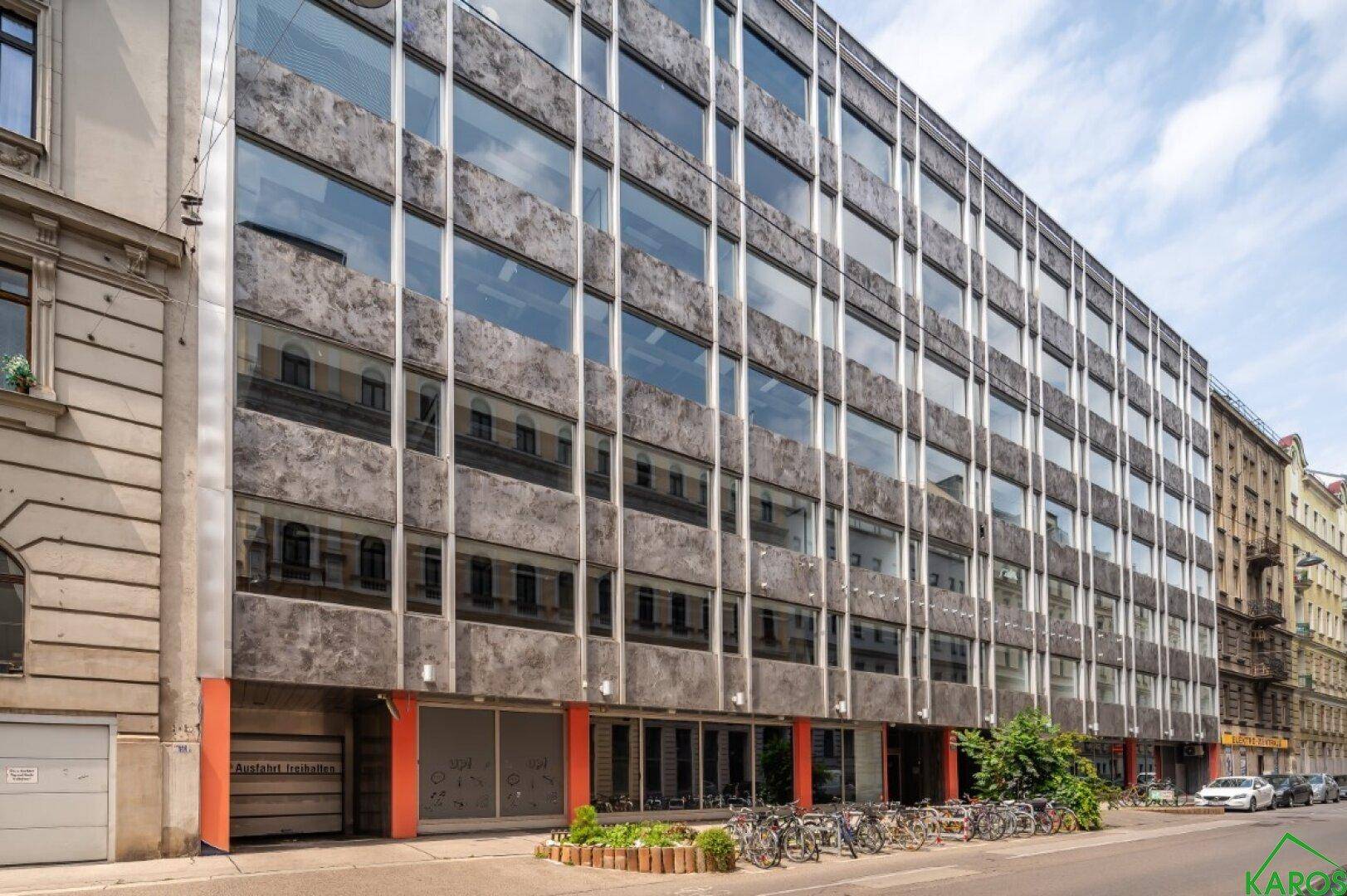 Modernes Bürogebäude mit großer Glasfassade und vielen Fenstern an einer Stadtstraße.
