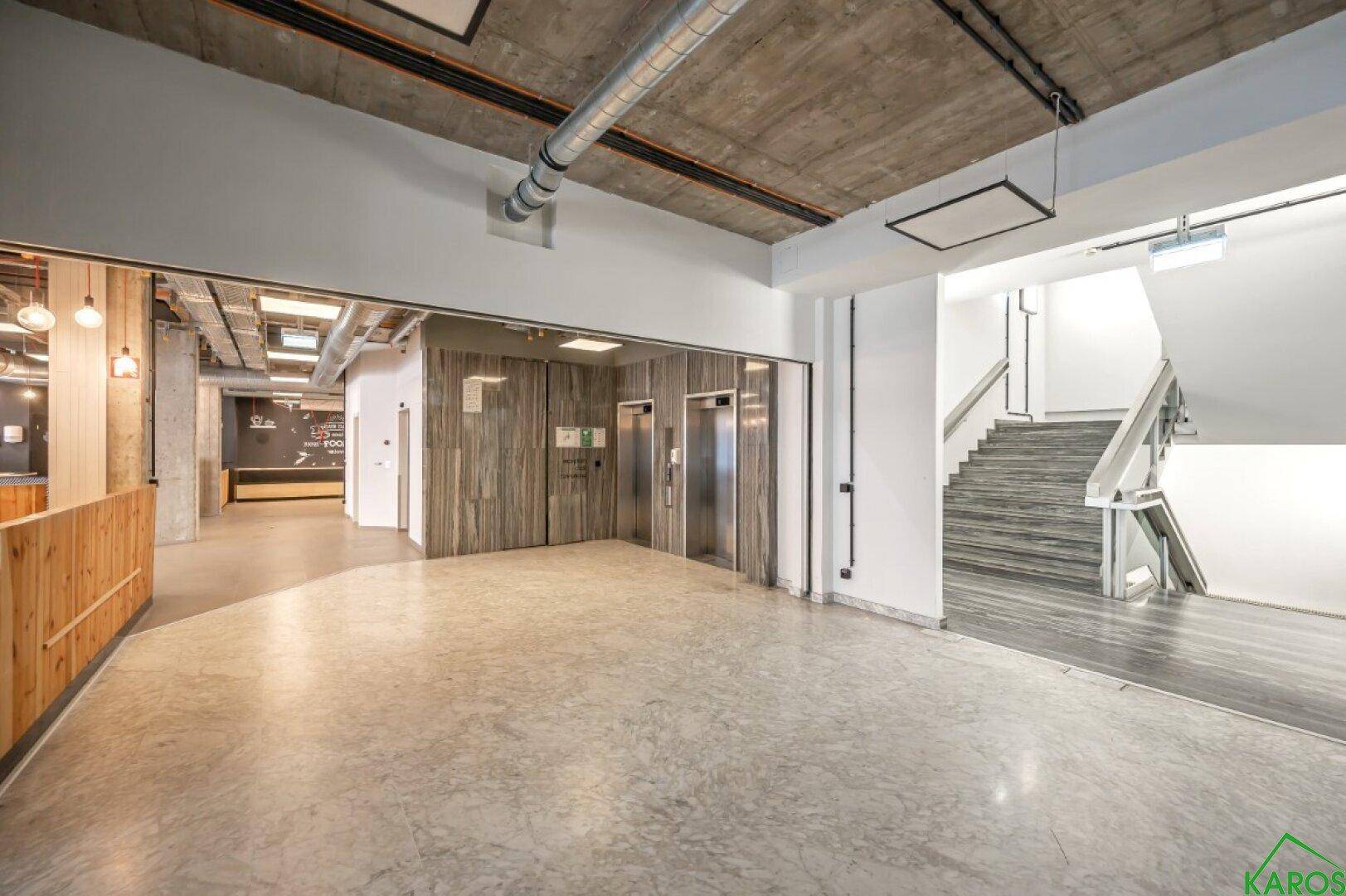 Geräumiger Eingangsbereich mit zwei Aufzügen, einer Treppe und industriellem Design.
