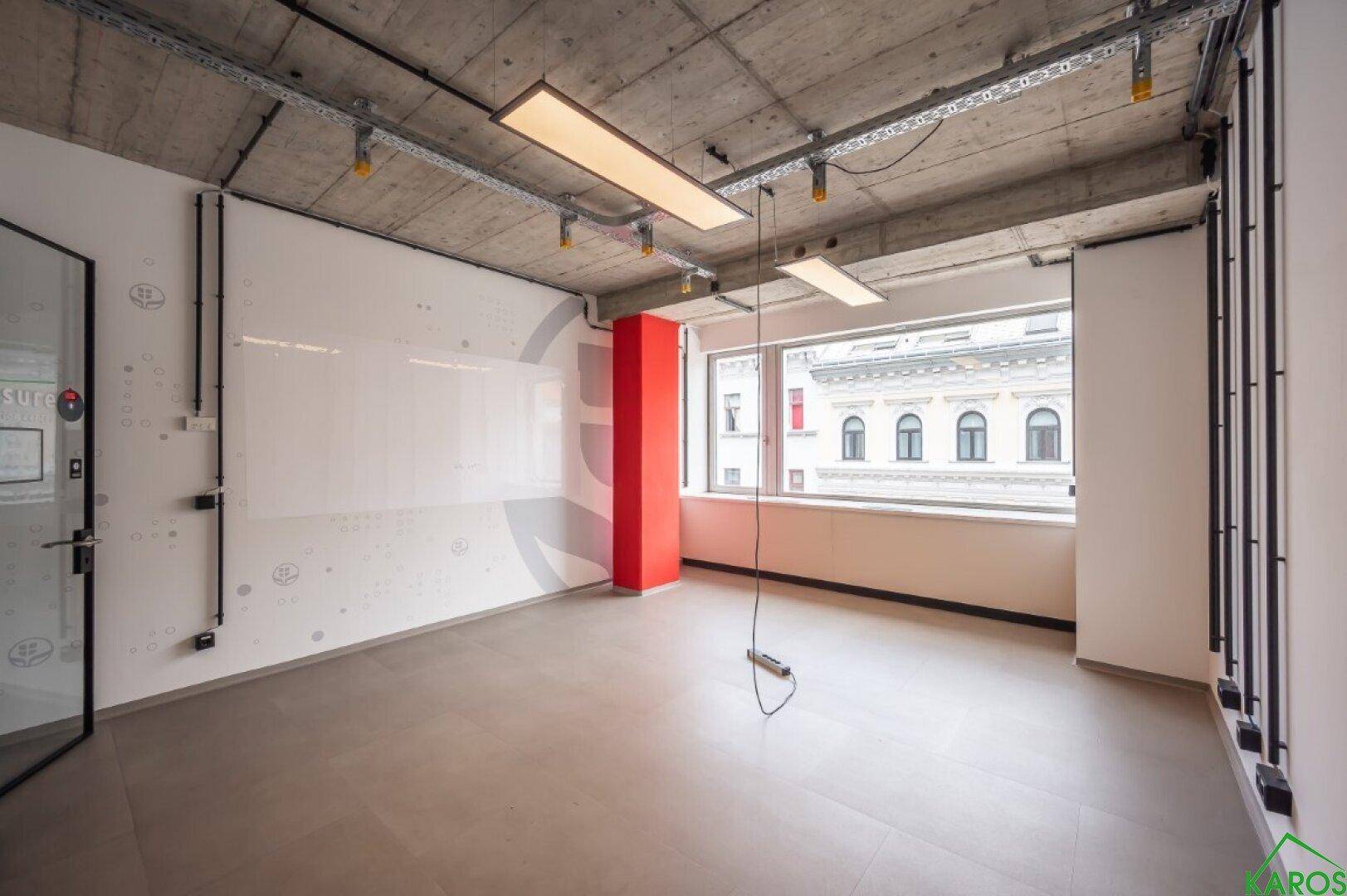 Helles Einzelbüro mit einem markanten roten Pfeiler und großen Fenstern für viel Tageslicht.