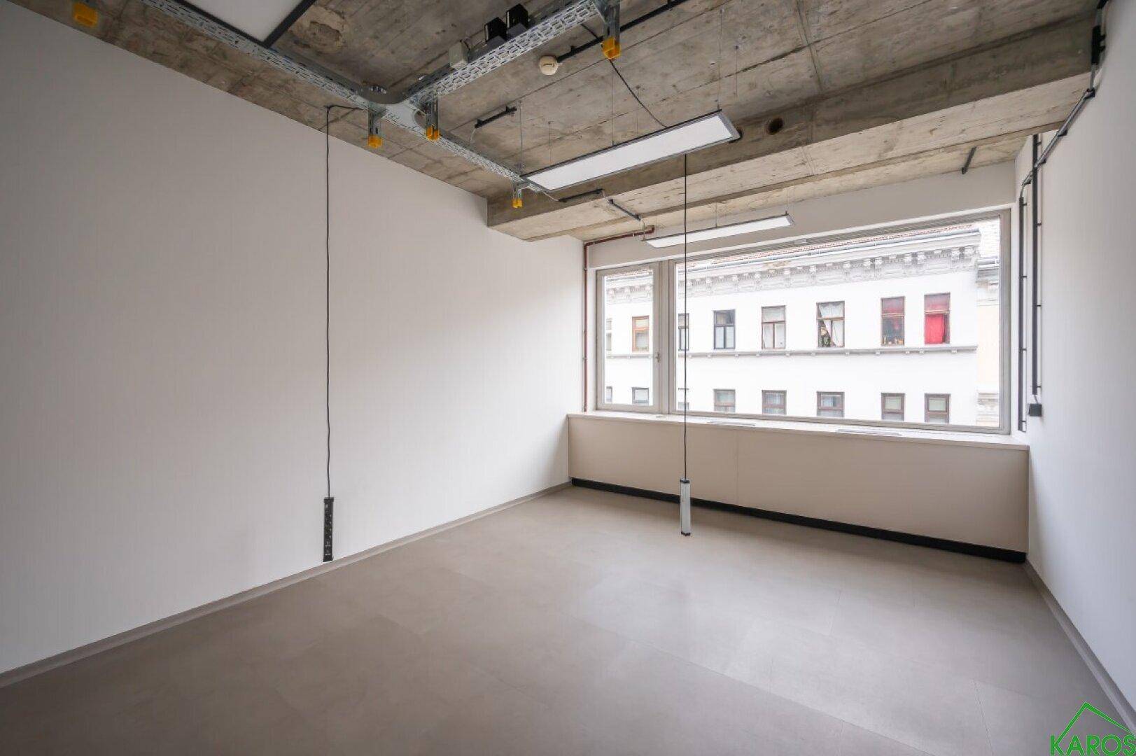 Schlichtes Büro mit großen Fenstern, die viel natürliches Licht hereinlassen, und hohen Decken.