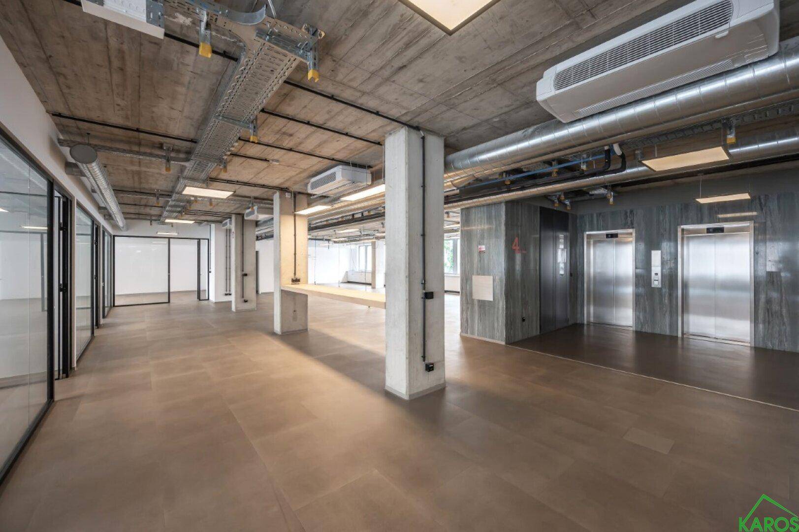 Große Bürofläche mit freiliegenden Decken, Säulen und Aufzügen im Hintergrund.